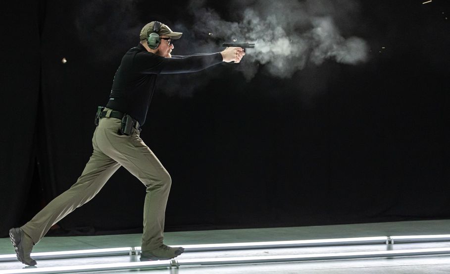 A sports shooter running through the shooting range, arms extended, aiming a pistol at a target with bullet casings flying through the air around him. The Edge in Sports Shooting: Insights from the Range