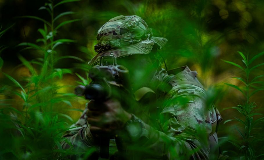 Operator in dense jungle foliage, aiming at a target with his firearm.